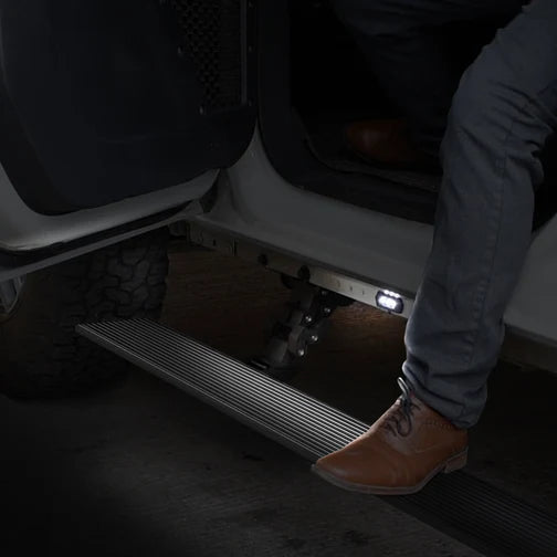 Go Rhino E1 electric running boards with LED lighting on Jeep Wrangler JL 4-door 2018-2025, showing retractable power steps.