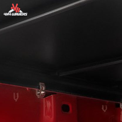 Close-up of a black truck bed liner or tonneau cover installed over a red truck bed, with a small metal clip fastening it.